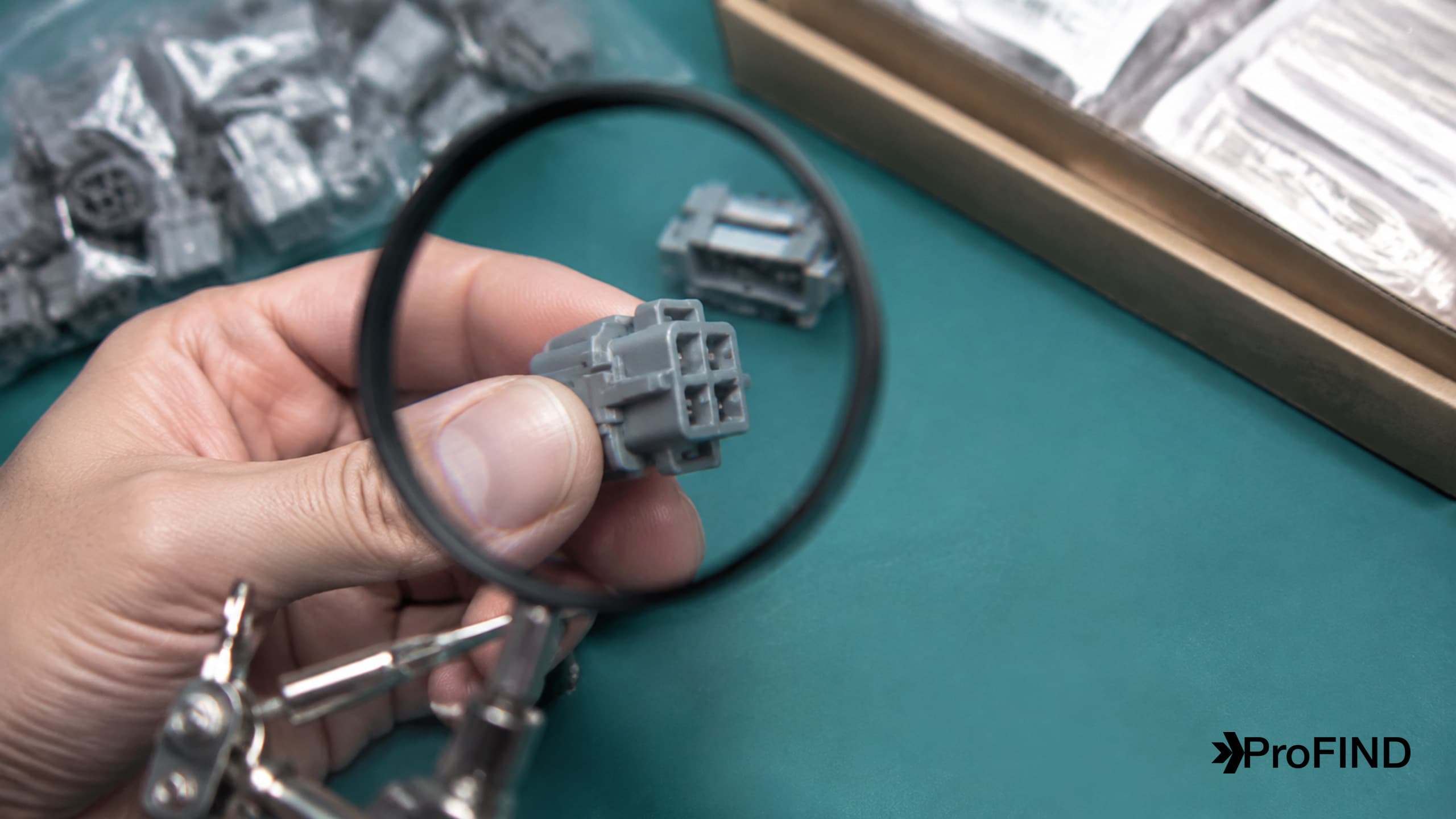 A hand examining a gray connector through a magnifying glass