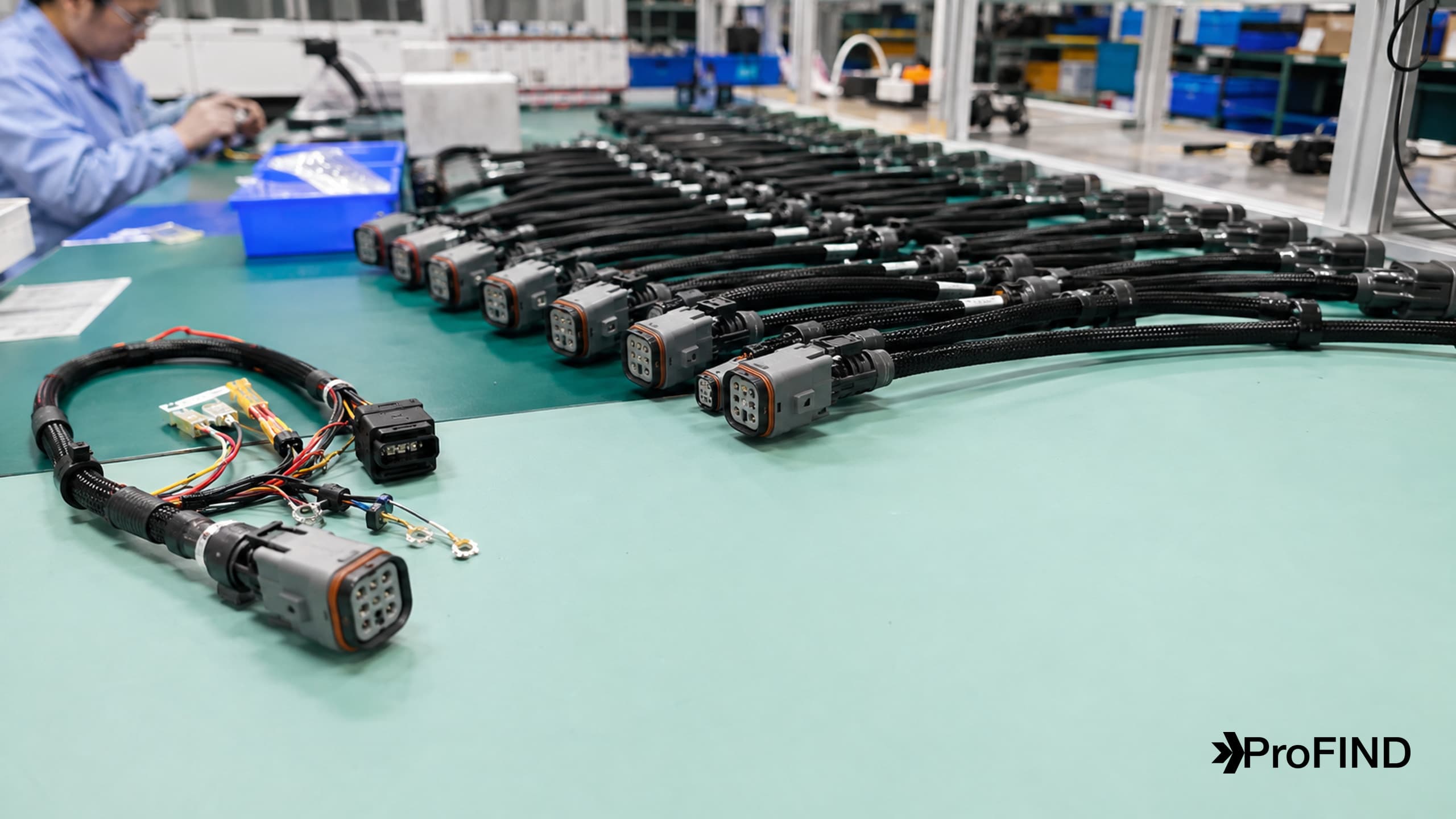 A prototype harness beside a row of consistently assembled production cable harnesses